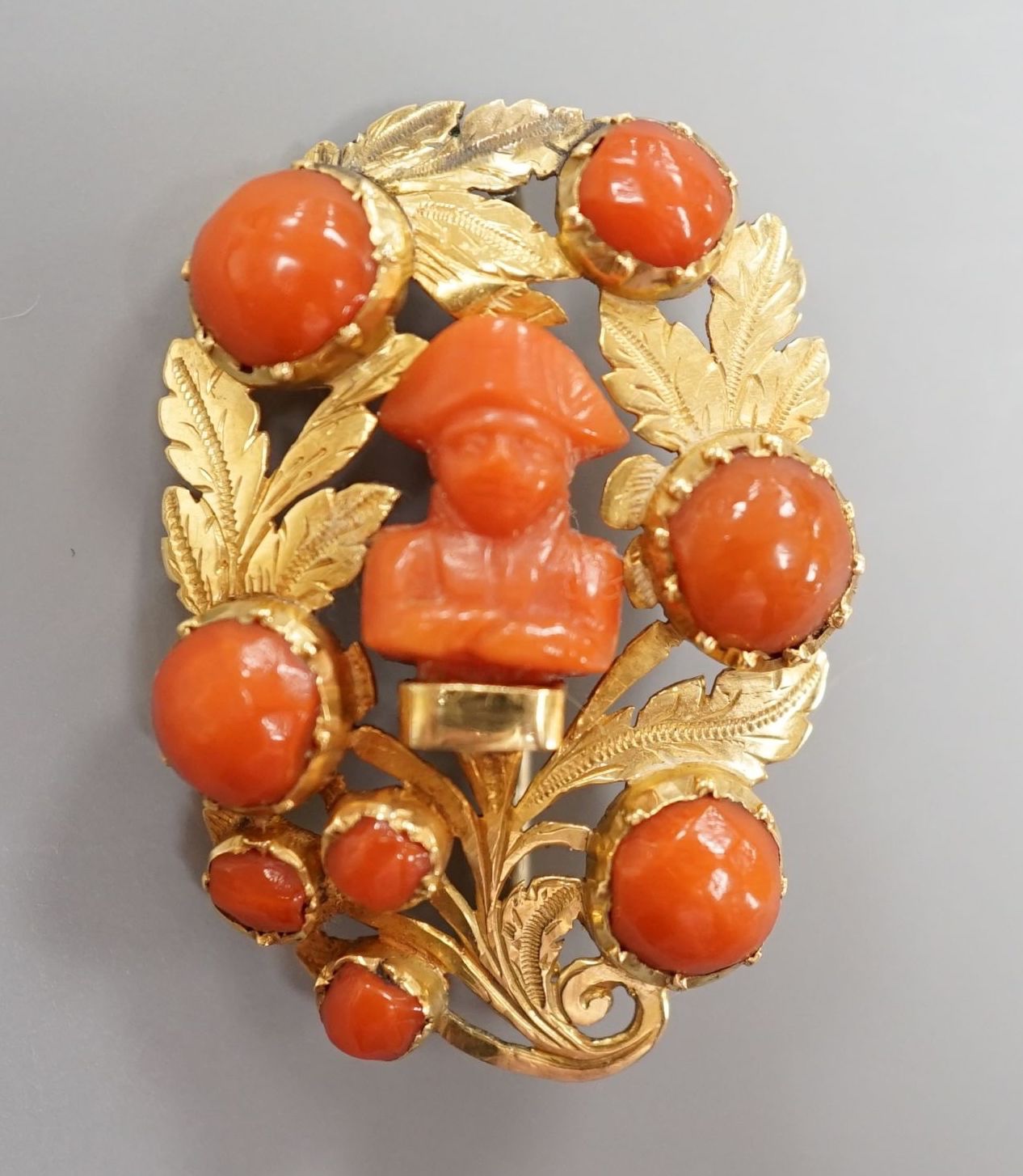 A 19th century yellow metal and coral set foliate brooch, the central motif carved as the bust of Napoleon, 37mm, gross weight 8.7 grams.